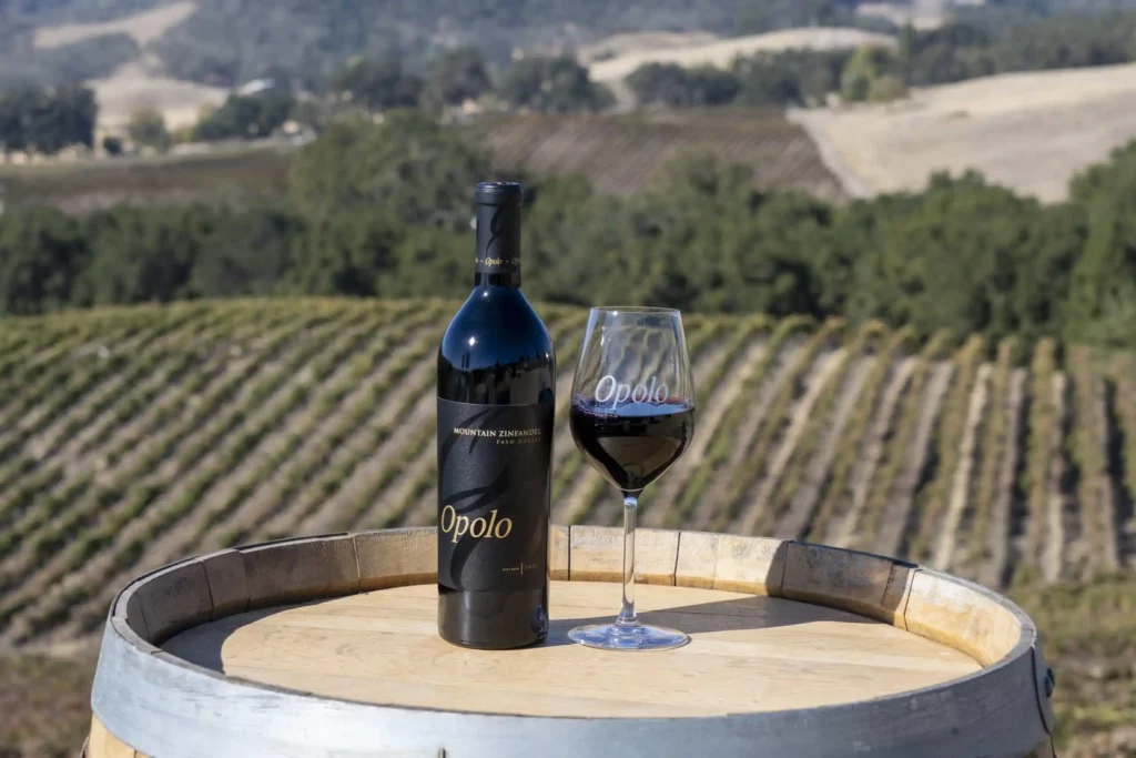 Bottle and glass of Opolo Mountain Zinfandel on a barrel with a view of the vineyard beyond